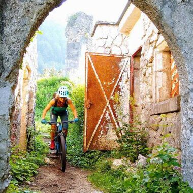 A woman rides her bike under a ruin