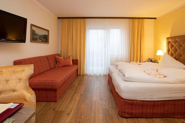 Ein Hotelzimmer im Hotel Agathawirt mit einem Doppelbett, einem roten Sofa  und einem Fernseher