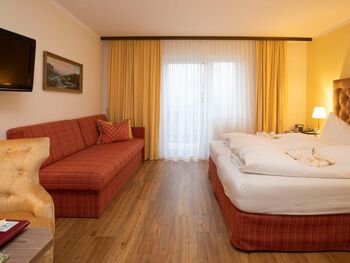 A hotel room at Hotel Agathawirt with a double bed, a red sofa and a TV set