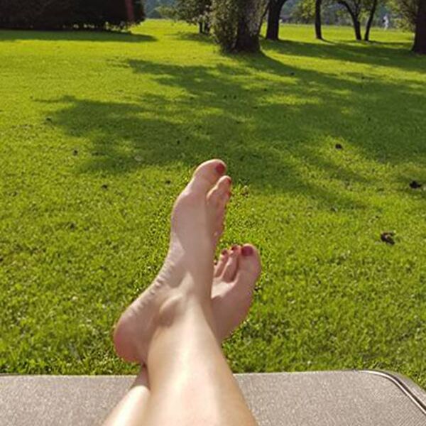 Eine Frau legt ihre Füße auf der Liege im Garten hoch