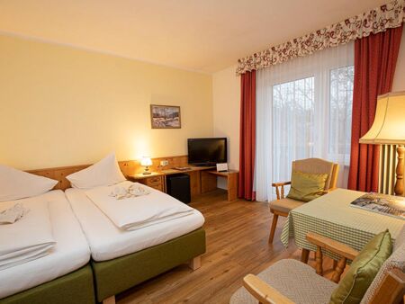 A double bed and two chairs with a table are in the hotel room of the Landhotel Agathawirt
