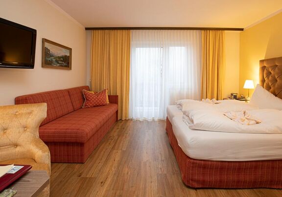 A hotel room at Hotel Agathawirt with a double bed, a red sofa and a TV set